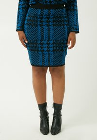 Falda de punto con estampado azul que presenta diseños geométricos en negro. Acompañada de botas negras hasta el tobillo con cremalleras y un acabado suave.
