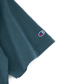 Ciemnozielona bawełniana koszulka z krótkim rękawem. Posiada małe haftowane logo w kolorze czerwonym i niebieskim na lewym rękawie. Gładka tekstura.