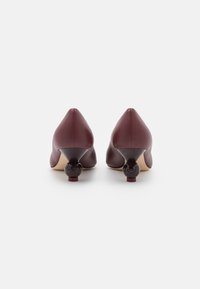 Chaussures à talons hauts en cuir bourgogne avec un bout pointu, présentant des accents de talon rond distincts et une texture lisse.
