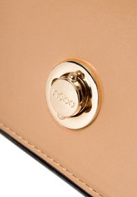 Bolso de piel marrón claro con un cierre circular dorado brillante y costuras negras en contraste. Textura suave con un diseño minimalista.
