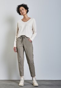 Lätt creamfärgad tröja med V-ringning, tillsammans med beige joggingsbyxor med elastiskt midjeband och sidofickor. Creamfärgade sneakers fulländar looken.