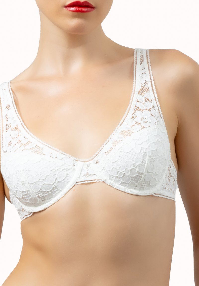 Femme portant un soutien-gorge en dentelle blanche avec des motifs floraux, visible du cou à la partie supérieure de l'abdomen, avec du rouge à lèvres rouge sur les lèvres.