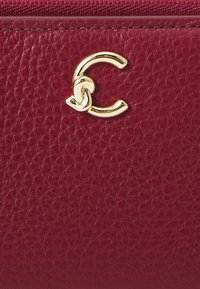 Portafoglio in pelle rossa con texture, caratterizzato da un accento con logo in lettere dorate. La superficie presenta una finitura a buccia di arancia con dettagli di cucitura sottili.