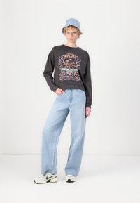 Black sweatshirt with a graphic print, paired with light blue wide-leg jeans. Model wears a light blue bucket hat and white sneakers.