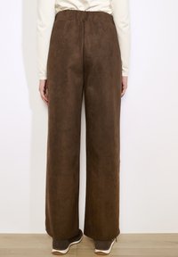 Br�ązowe spodnie o szerokich nogawkach, wykonane z miękkiego, zamszopodobnego materiału, z elastycznym paskiem w talii, charakteryzujące się gładką fakturą i prostym wzornictwem.