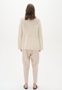 Beige strikket sweater med løs pasform, struktureret mønster og ribbet kant, parret med lyse beige skræddersyede bukser og flade sorte sandaler.
