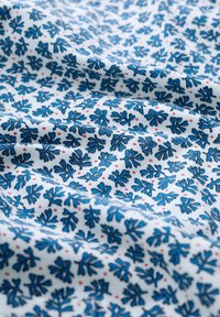 Puuvillakangas, jossa on sininen lehtikuvio ja satunnaisia punaisia pisteitä vaaleansinisellä taustalla. Pehmeä rakenne ja laskostettu ulkonäkö.