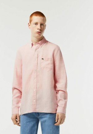 Camisa de manga larga de color rosa claro con botones y un bolsillo en el pecho, hecha de una tela texturizada, que presenta un pequeño logo bordado en negro.