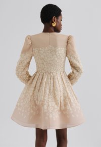 Vestito a maniche corte, lunghezza ginocchio in beige morbido con stampa leopardo chiara, gonna plissettata e dettaglio della zip a occhiello sulla schiena.