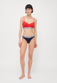 Czerwony usztywniany stanik z regulowanymi ramiączkami oraz czarno-białą taśmą z logo. Pasujące granatowe majtki bikini z elastyczną taśmą z logo.