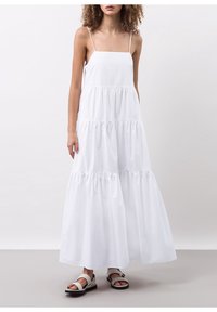 Bílé maxi šaty s tenkými ramínky, s volánky ve vrstvách a splývavým střihem. V kombinaci s plochými sandály s širokým popruhem a přezkou.