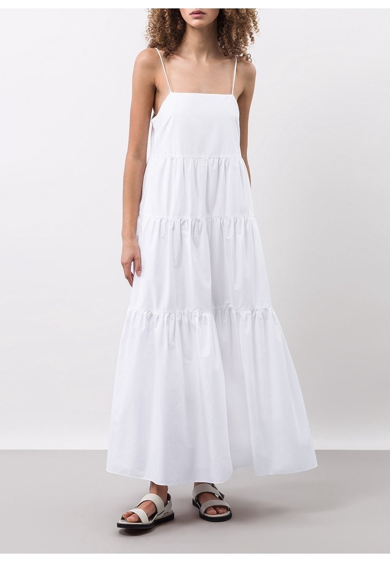Bílé maxi šaty s tenkými ramínky, s volánky ve vrstvách a splývavým střihem. V kombinaci s plochými sandály s širokým popruhem a přezkou.