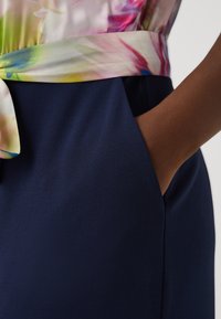 Haut fluide avec un motif floral dans des couleurs pastel douces au-dessus d'une jupe bleu marine avec une texture lisse et une poche sur le côté.