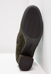 Zapato de ante verde con punta redonda, suela de goma negra y agarre texturizado. Presenta un cierre lateral para facilitar su colocación. Marcado "Gabor" en la parte inferior.