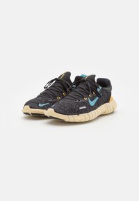 Une paire de chaussures de sport noires et beiges avec des logos swoosh bleus et une texture tricotée détaillée, présentée côte à côte sur un fond blanc.