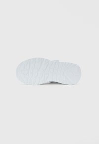 Suola di una sneaker bianca che mostra motivi di battistrada geometrici su uno sfondo chiaro e uniforme.