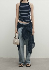 Canottiera a righe blu navy e bianche con scollo quadrato, jeans a gamba larga blu chiaro, camicia a righe blu navy annodata e borsa beige.