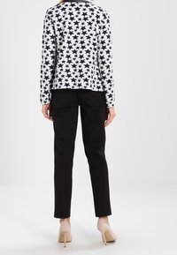 Langarmshirt met een marineblauw-witte sterrenprint, gecombineerd met zwarte, op maat gemaakte pantalon. De outfit wordt compleet gemaakt met naakte hoge hakken.