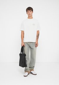 Hvit kortermet t-skjorte med en sirkulær grafikk på brystet, parret med lysvaskede jeans og svart tote-bag med solide stropper.
