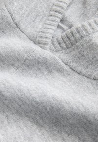 Szürke kötött pulóveranyag közeli felvétel, V-nyakkivágással, bordázott textúrával és puha, sima gyapjúkeverék felülettel.