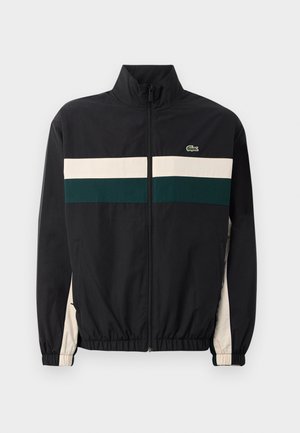 Chaqueta negra con cuello alto, con rayas horizontales verde y crema. El material parece ligero; incluye puños elásticos y un logotipo.