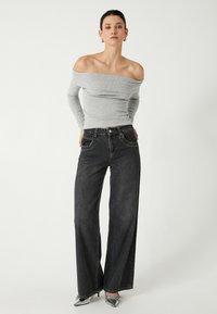 Top grigio a spalle scoperte con maniche lunghe abbinato a jeans neri a vita alta con gamba larga e scarpe con tacco alto argento. Design semplice e moderno.