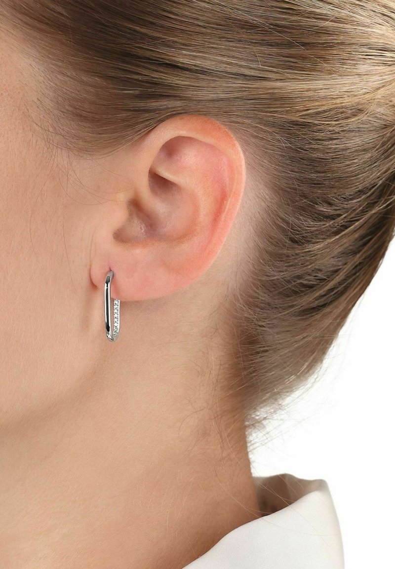 Orecchino a cerchio in argento con un design sottile e una fila di piccoli gemelli trasparenti lungo il bordo anteriore, esposto su un orecchio.