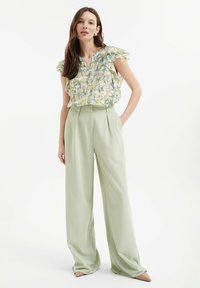 Bloes met bloemenpatroon in groen, geel en wit; met gerimpelde mouwen. Lichtgroene, high-waisted, wijde broek met een zachte textuur.