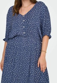 Abito floreale blu con scollatura a V, maniche corte, dettagli a bottoni e vita arricciata, realizzato in un tessuto leggero con un motivo testurizzato.