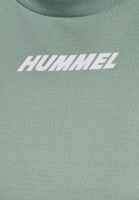 Green, fitted t-shirt made of textured fabric, featuring a white "HUMMEL" logo across the chest. Simple, crew neck design.