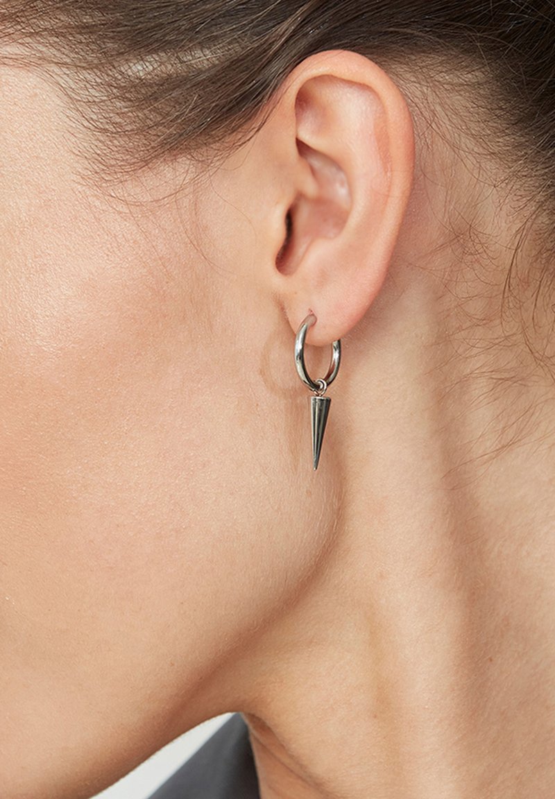 Sudrabaini auskari ar norādītu piekariņu, kas ir ar pulētu apdari un gludu tekstūru. Vienkārša, moderna dizaina pieeja, kas koncentrējas uz ģeometriskām formām.