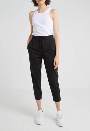 Débardeur blanc à côtes et pantalon noir fuselé avec poches latérales et ceinture à cordon, associé à des sneakers à plateforme blanches.