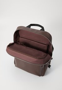 Brown backpack with a textured exterior, full-length zipper, and a compartmentalized interior. Features a top handle and padded sections.