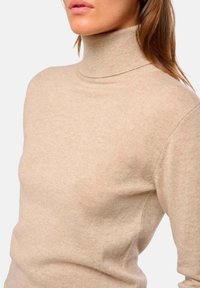 Pull col roulé beige clair en tricot doux ; design ajusté avec col côtelé et épaules sans coutures. Texture lisse, détails minimaux.