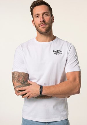 Witte katoenen T-shirt met ronde hals, featuring een zwart bedrukt logo "BANDERA RODEO TEXAS" op de borst. Model met zichtbare tatoeages en armband.