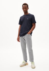 T-shirt col rond bleu marine en coton, associé à un jean droit gris clair et des baskets multicolores avec des accents verts.