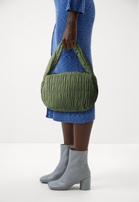 Fjäderlätt grön handväska med quiltat mönster och rundade handtag, parat med en blå ribbad klänning och ljusgrå ankelstövlar med blockklack.