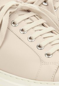 Helle beige Sneaker aus strukturiertem Leder, mit runder Zehenform, silbernen Ösen und flachen cremefarbenen Schnürsenkeln. Stickdetails entlang der Seiten.