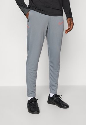 Sive sportske hlače slim kroja, s narančastim Nike logotipom i džepovima na zip; napravljene od glatkog, laganog materijala.