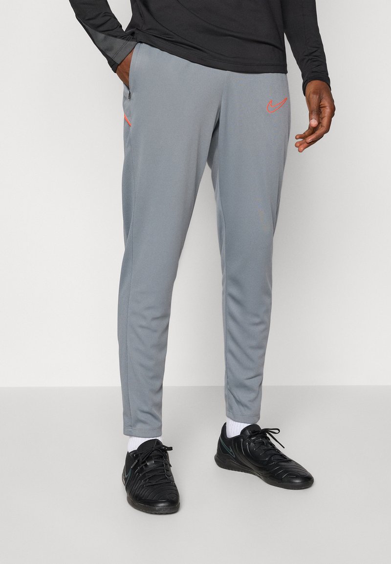 Gray athletic pants with a slim fit, featuring an orange Nike logo and zippered pockets; made of smooth, lightweight fabric.