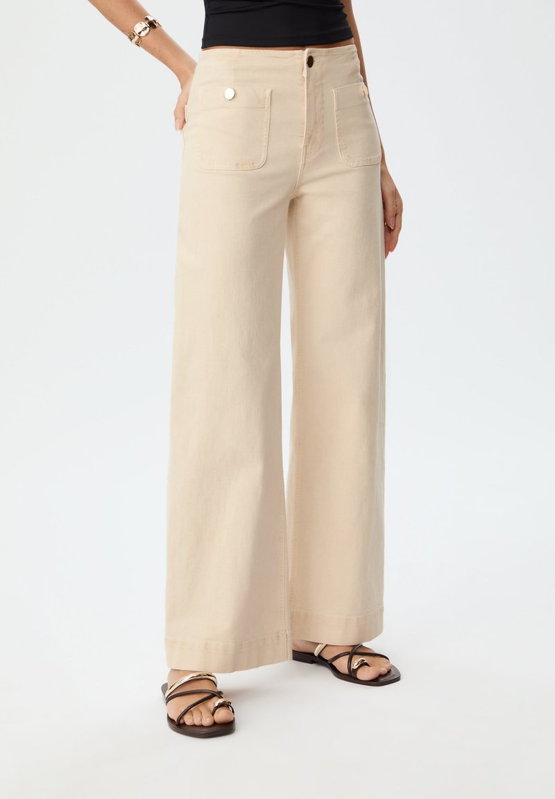 Beige wijde broek gemaakt van katoen, met twee voorkruiszakken, een hoge taille en een nette, naadloze afwerking aan de onderkant.