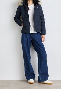 Navy puffer jacket with a fur-lined hood, paired with wide-leg denim jeans and white sneakers with yellow soles.