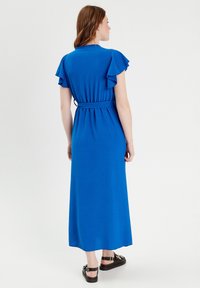 Robe maxi bleue avec des manches courtes à volants, une taille ceinturée et une texture lisse. Conçue avec une silhouette longue jusqu'au sol.