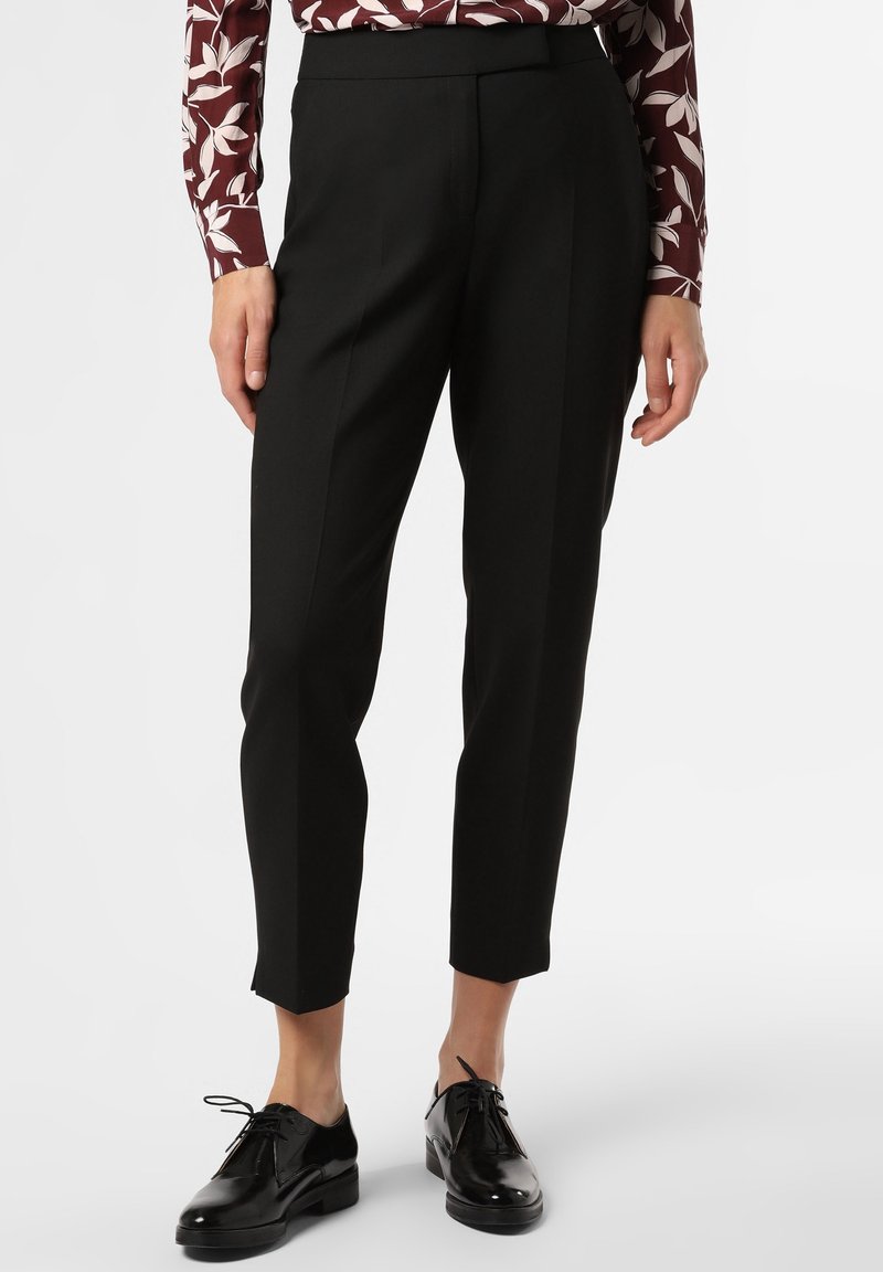 Svarta skräddarsydda byxor med smal passform, som har en slät yta och veckdetaljer, tillsammans med glänsande svarta skor.