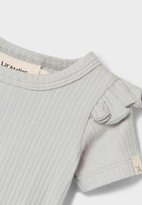 Grå, ribbet stoff med rund halslinning og volangdetaljer på ermene. Et vevet merke er synlig på sidesømmen. Strukturert overflate.