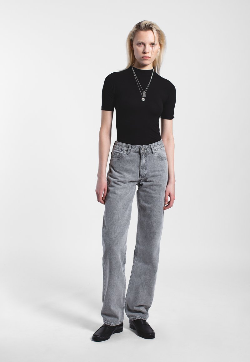 Top nero a maniche corte abbinato a jeans grigi chiari a vita alta. La modella indossa collane in argento a strati e scarpe nere con tacco basso.