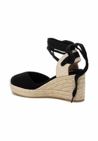 Espadrilles de cuña de ante negro con tacón texturizado de color crema, punta cerrada y cordones negros que envuelven el tobillo. Suela intermedia de yute trenzado.