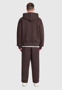 Brązowa bluza z dużym kapturem z tyłu oraz dopasowane luźne spodnie. Miękka tkanina z żebrowanymi mankietami i dołem. Biała koszulka widoczna w pasie.
