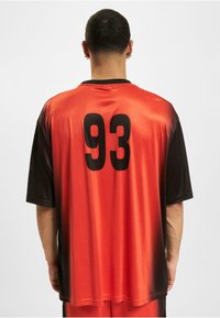 T-shirt med korte ærmer lavet af glat stof, med en orange til sort gradient og et stort sort "93" på ryggen.