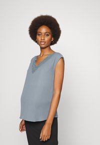 Top sem mangas azul claro com decote em V e renda, apresentando um corte solto e uma textura suave, combinado com uma parte de baixo riscada em preto.